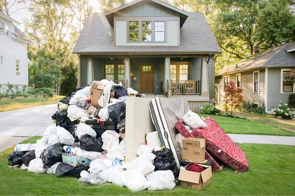 Large pile of household junk, trash bags, old mattresses, and cardboard boxes stacked on the front lawn of a suburban house Junk and Clutter Removal in Seattle Area WA